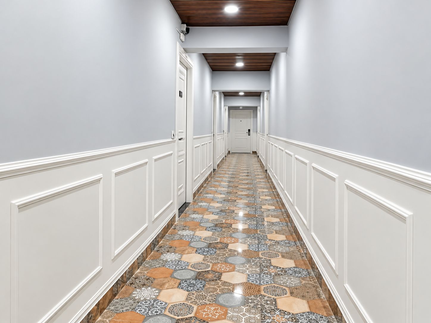 A hallway with patterned flooring, white walls, and a wooden ceiling.