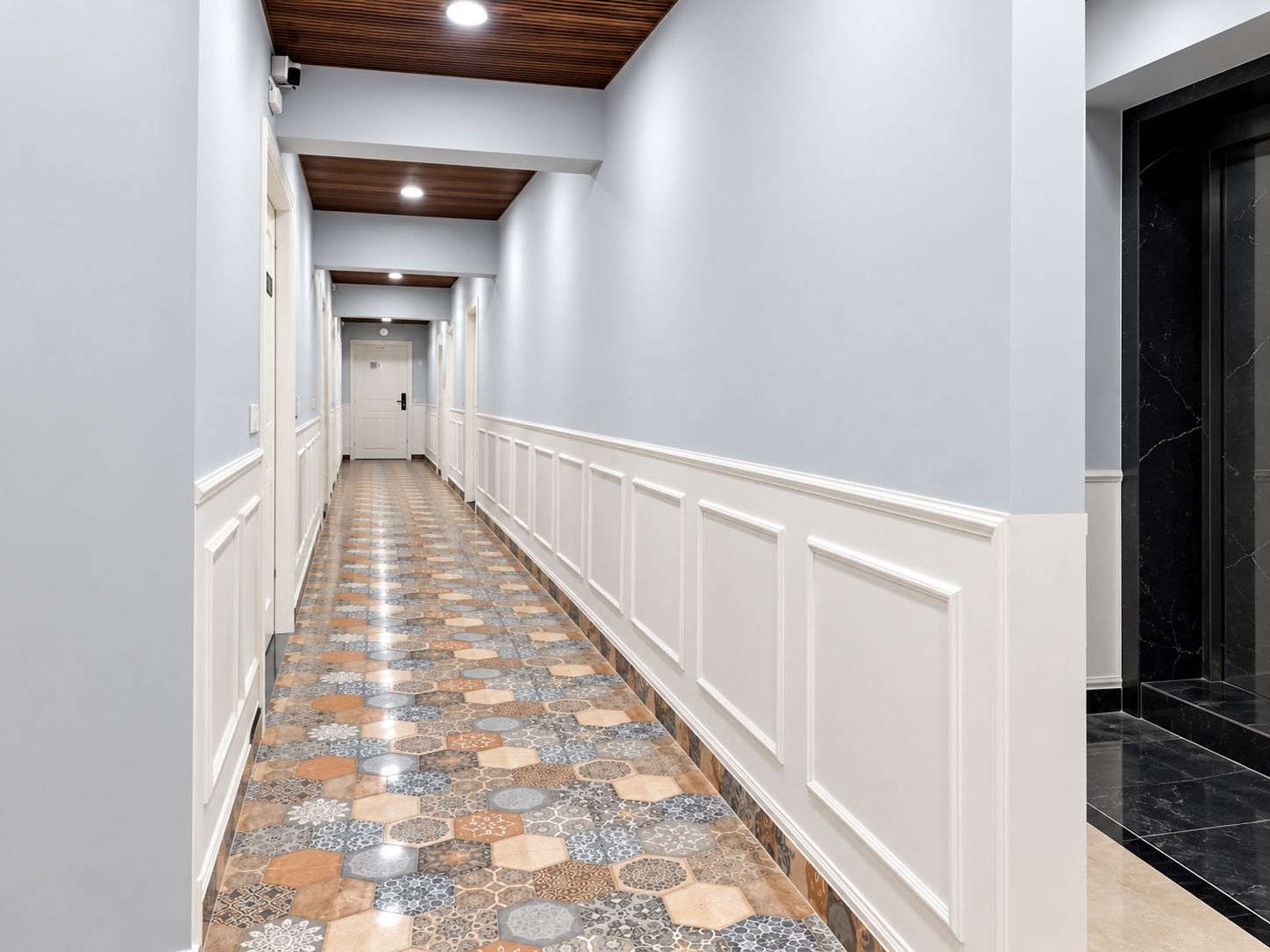 A hallway with patterned flooring, white wainscoting, and a black marble staircase.