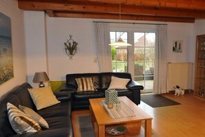 A living room with a black leather sofa, a wooden coffee table, and a dog. - Holiday home in Hooksiel with swimming pool (Hooksiel)