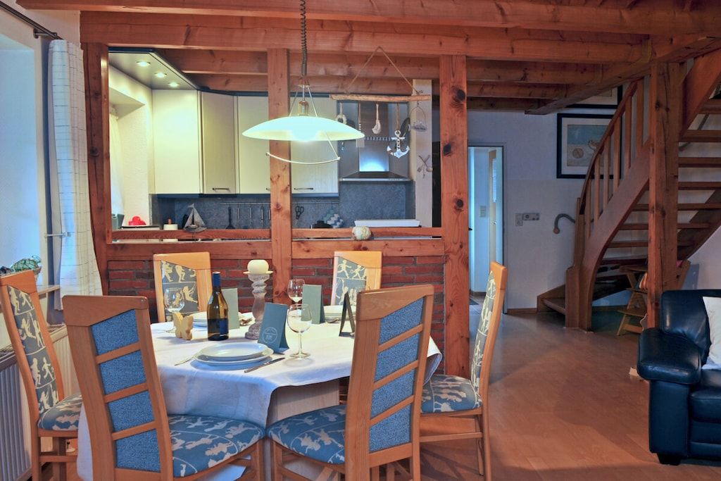 Een eetruimte met een tafel voor vier personen, houten stoelen, een hanglamp en uitzicht op de keuken.