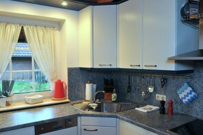 A kitchen with white cabinets, a granite countertop, a window with curtains, and various kitchen utensils. - Holiday home in Hooksiel with swimming pool (Hooksiel)