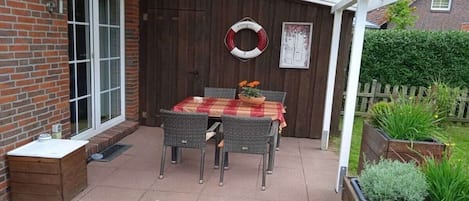 Eine Terrasse mit Tisch und Stühlen, eine Holztür und ein Gartenbereich mit Pflanzen.