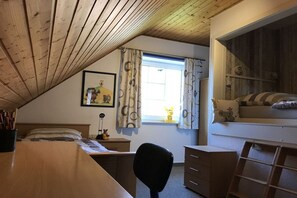 A room with a sloped ceiling, a desk with a chair, a bed with a window, and a dresser. - Holiday home in Hooksiel with swimming pool (Hooksiel)