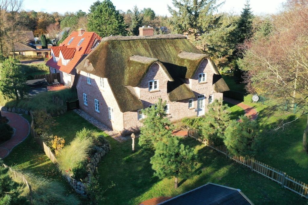Une maison traditionnelle avec un toit de chaume, entourée d’un jardin bien entretenu et d’une clôture en bois.