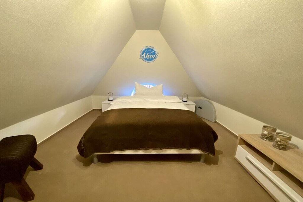 Ein kleines, dreieckiges Schlafzimmer im Dachgeschoss mit einem Bett, Nachttischen und einem an der Wand befestigten Schild.