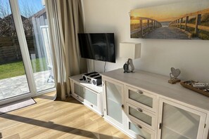 Ein Zimmer mit Fernseher auf einem Schrank, einem Schubladenschrank, einem Strandbild und einer Glastür zum Außenbereich.
