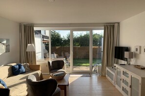 A spacious living room with a sofa, armchair, and a television. There is a sliding glass door leading to an outdoor area. - Holiday apartment with 2 bedrooms (Langeoog)