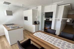 Eine kompakte Küche mit Spüle, Mikrowelle und Kaffeemaschine. Es gibt einen Essbereich mit Tisch und Stühlen.