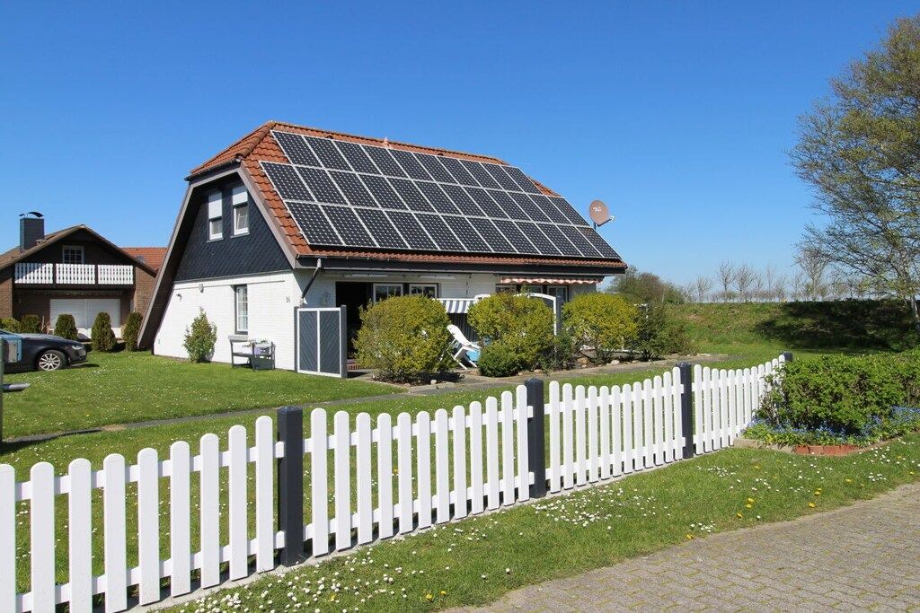 Une maison avec un toit en pente, des panneaux solaires, une clôture blanche en bois et une pelouse bien entretenue.