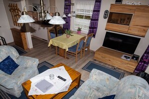 Een compacte woonruimte met een eethoek, een zithoek, een televisie en een houten kast.