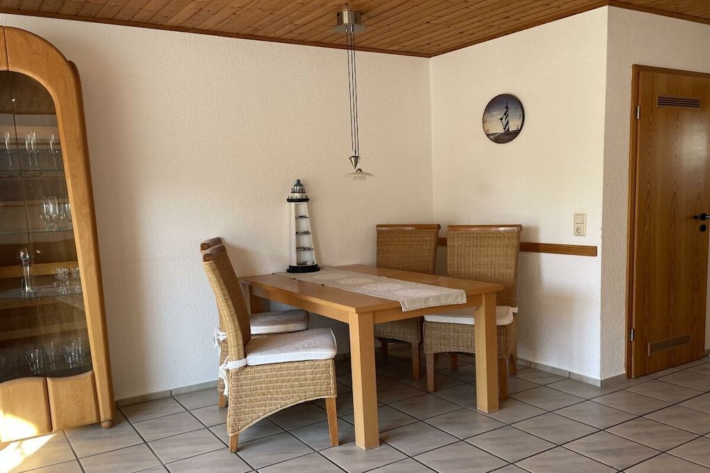 Ein Essbereich mit Holztisch, Korbstühlen, einer Wanduhr und einer Tür.