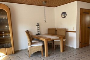A dining area with a wooden table, wicker chairs, a wall clock, and a door. - Holiday home with 2 bedrooms (Norddeich)