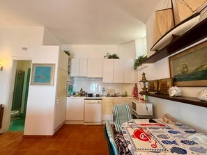 A compact kitchen with white cabinets, a microwave, and a dining area with a table set for two. - Casa Amanda: A Window onto the Sea in the Portofino Marine Park (Pedale)