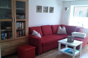 Ein rotes Sofa mit passendem Hocker, ein weißer Beistelltisch und eine Holzkommode mit Glastüren.