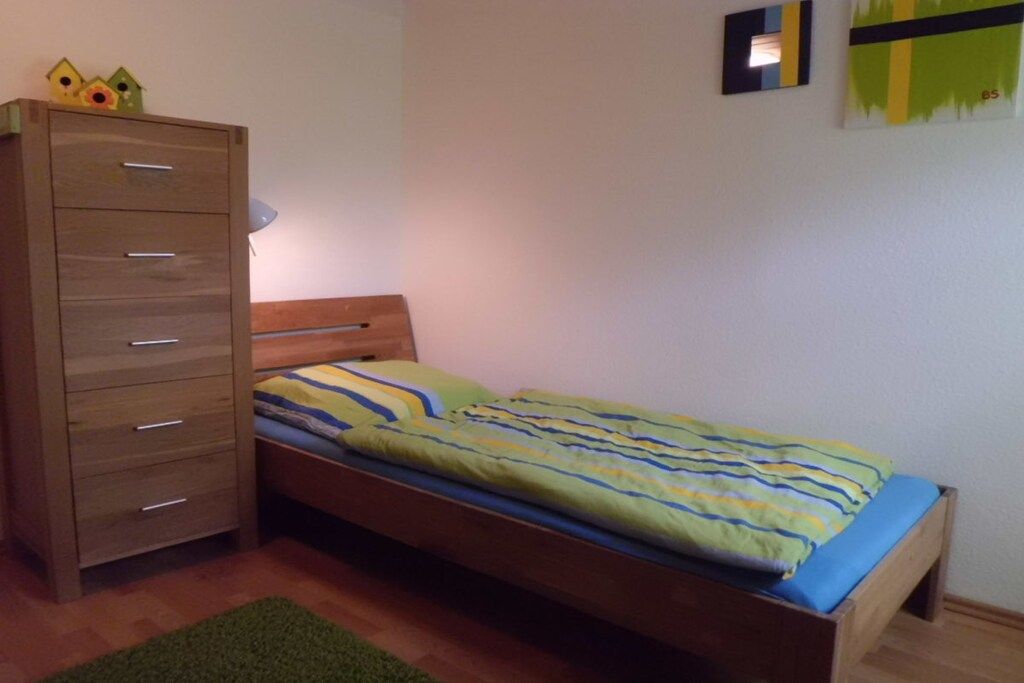 A single bed with a wooden headboard and a green and blue striped bedspread.