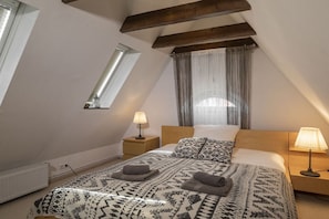 A bedroom with a sloped ceiling, a bed with patterned bedding, two bedside lamps, and a window with curtains. - Holiday home with 3 bedrooms (Lübeck Travemünde)