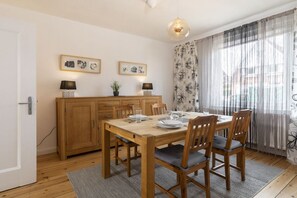 A dining area with a wooden table, chairs, and a cabinet. There are two wall-mounted lamps and framed pictures above the cabinet. - Holiday home with 3 bedrooms (Lübeck Travemünde)