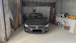 A car parked in a garage with concrete walls, wooden planks, and various items on shelves. - Penthouse · 100 m² terrace · Jacuzzi (Saranda)
