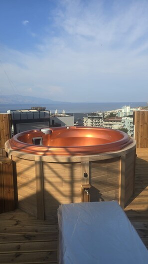 A hot tub on a wooden deck with a view of the ocean and buildings in the background. - Penthouse · 100 m² terrace · Jacuzzi (Saranda)