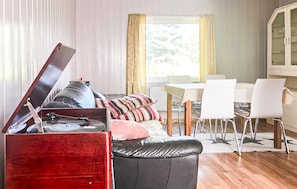 A living room with a red cabinet, a black leather sofa, a dining table with white chairs, and a window with curtains.