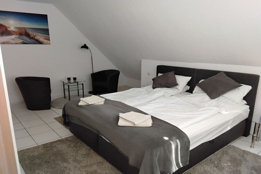 Une chambre à coucher avec un lit, des tables de chevet, une chaise et une poubelle.