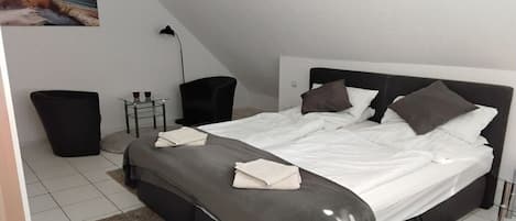 A bedroom with a bed, bedside tables, a chair, and a trash bin.