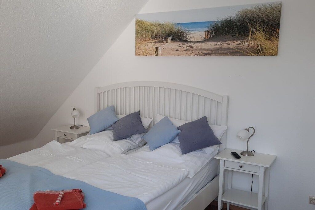 A bedroom with a bed, pillows, a bedside table with a lamp, and a wall-mounted picture of a beach.