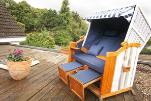 A wooden deck with a wicker lounge chair and a potted plant. - Holiday apartment with 3 bedrooms (Lübeck)