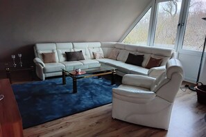 Ein modernes Wohnzimmer mit einem weißen Ecksofa, einem Glastisch und einem blauen Teppich.