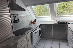 Eine kleine Küche mit integriertem Waschmaschinenanschluss, einem Fenster für Tageslicht und Blick ins Grüne.