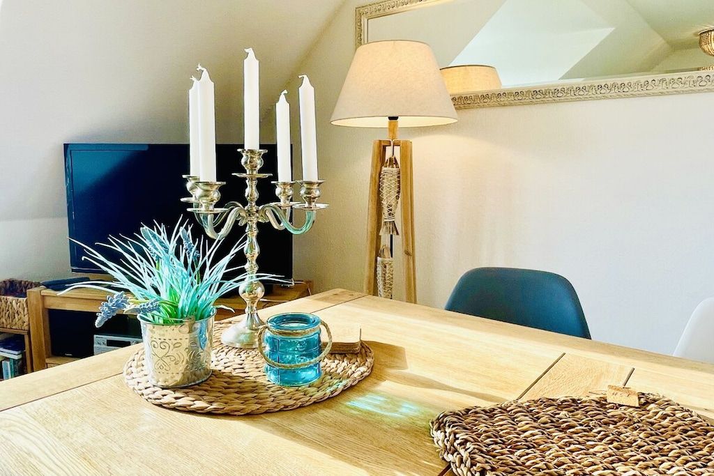 Un coin repas avec une table en bois, un chandelier avec des bougies, une lampe et un set de table en fibres tressées.