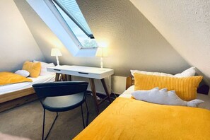 A small, triangular room with a bed, a desk, and a chair. There is a skylight above the desk. - Holiday apartment with 1 bedroom (Boltenhagen)