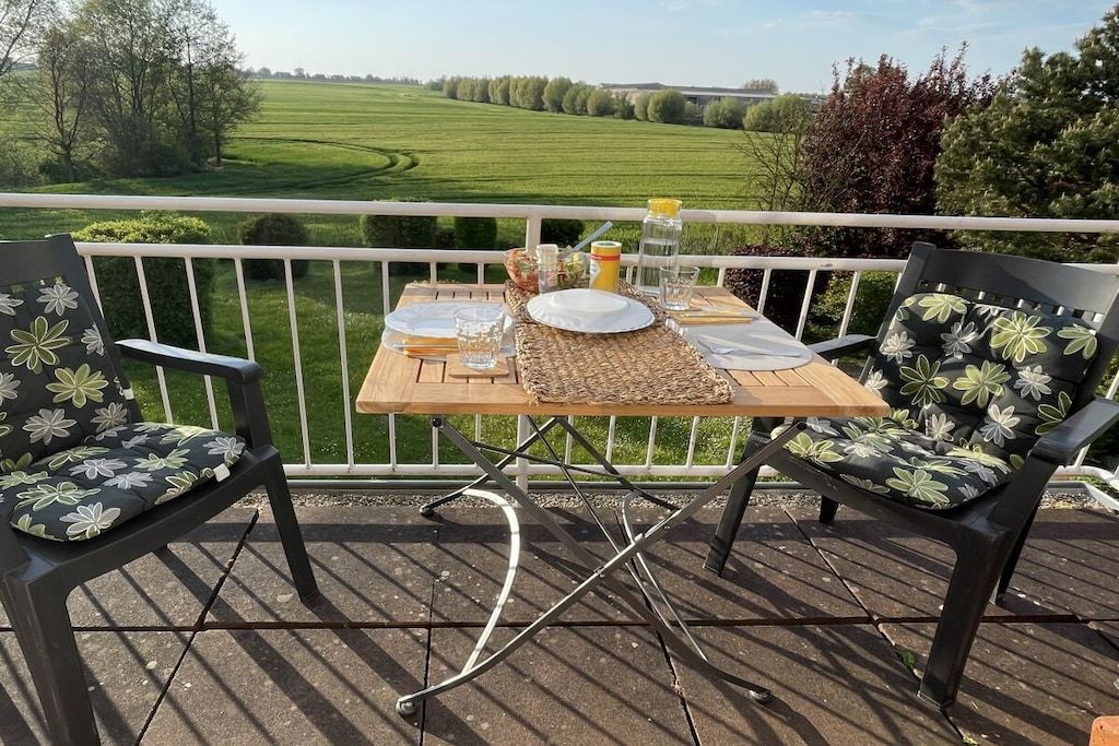 A wooden deck with a table set for two, surrounded by chairs with floral upholstery.