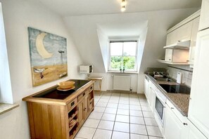 Eine Küche mit einer Holzausziehtafel, weißen Schränken, einem Fenster mit Blick und einem Halbmond-Gemälde an der Wand.