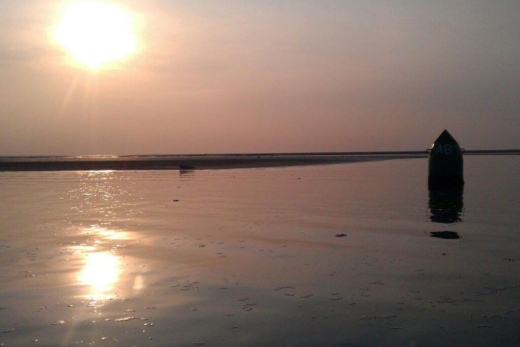 Escena de platja amb cel serè i el sol baix a l'horitzó, reflectint sobre la sorra mullada.