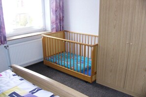 A room with a wooden crib, a radiator, a window with curtains, and a wardrobe. - 3 ( OR) with balcony "House Sloop" (Dornumersiel)