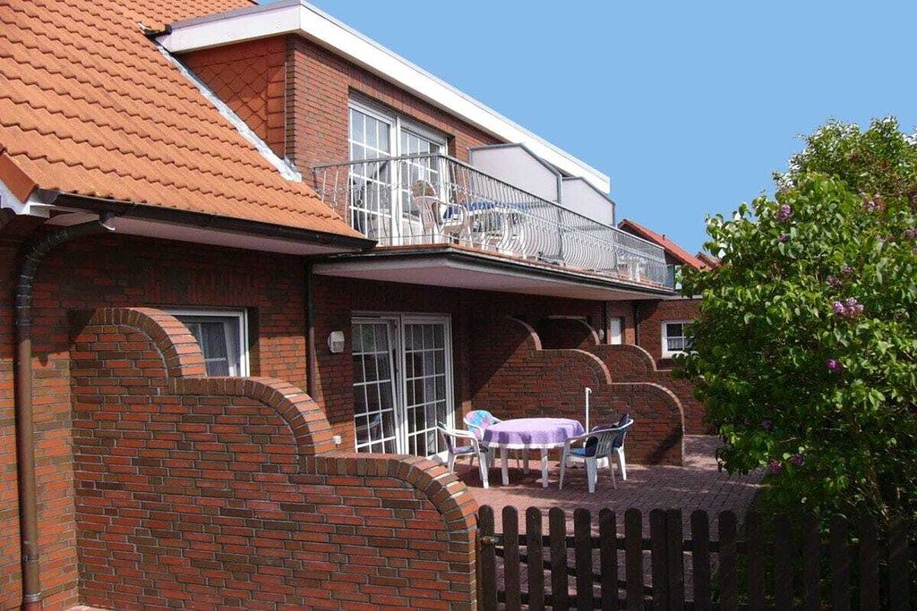 Une maison en briques avec un balcon, une cour clôturée et une table avec des chaises.