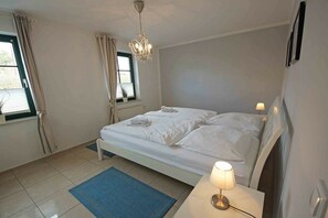 A bedroom with a bed, bedside lamps, a chandelier, a window with curtains, and a blue rug. - Holiday apartment with 2 bedrooms (Prerow)