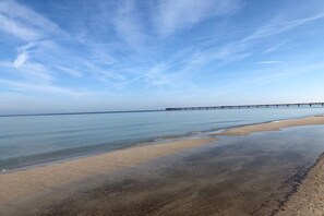 Ein Strand mit einem Steg, der sich in ruhiges Wasser unter einem klaren Himmel erstreckt.
