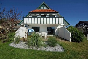 A two-story house with a red-tiled roof, white exterior walls, and a small front porch with chairs. - Holiday apartment with 2 bedrooms (Prerow)