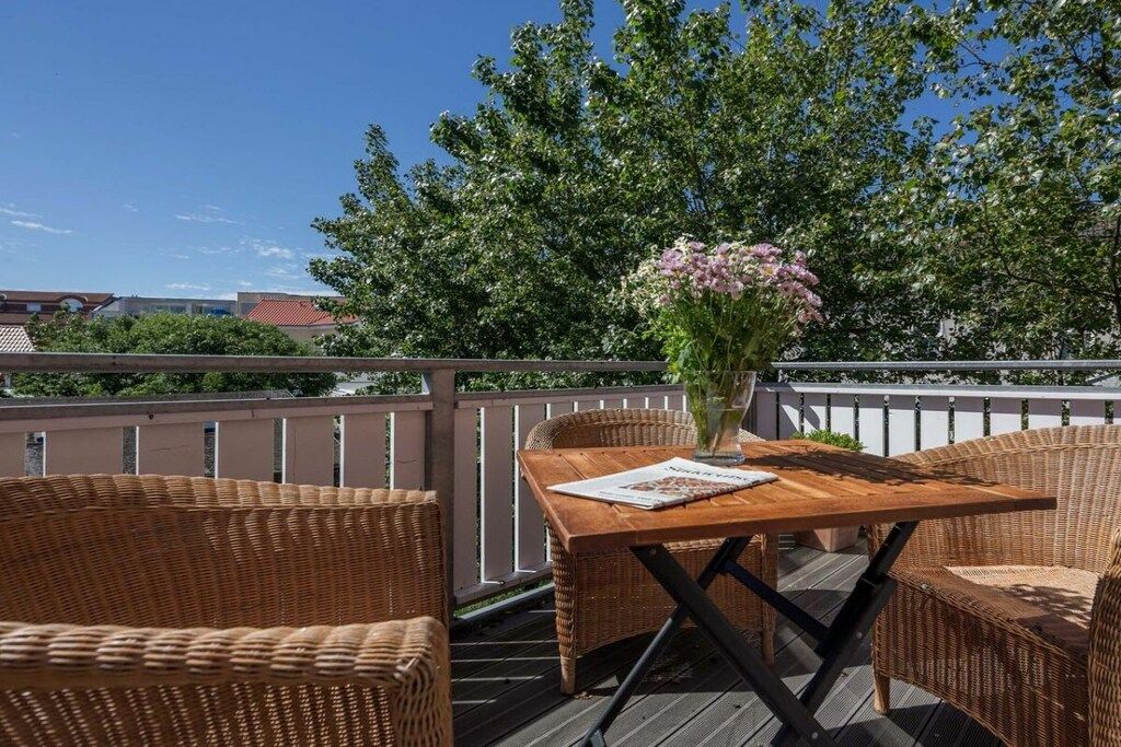 A wooden deck with wicker furniture and a vase of flowers.
