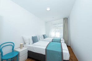 Una camera da letto con due letti, un comodino, una sedia e una finestra con tende.