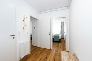 A hallway with white walls, a wooden floor, and a bed with a teal blanket in the background. - Marvien - City Stay - Modern 2BR Apartment - Free Garage (Vienna)