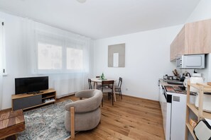 Un appartement moderne doté d’une télévision à écran plat, d’un coin repas, d’une cuisine équipée d’un four à micro-ondes et d’une grande fenêtre.