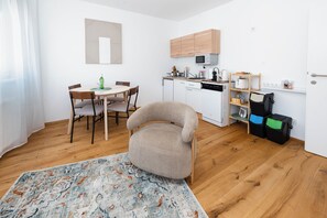 A compact living space with a dining area, kitchenette, and a seating area with a chair. - Marvien - City Stay - Modern 2BR Apartment - Free Garage (Vienna)