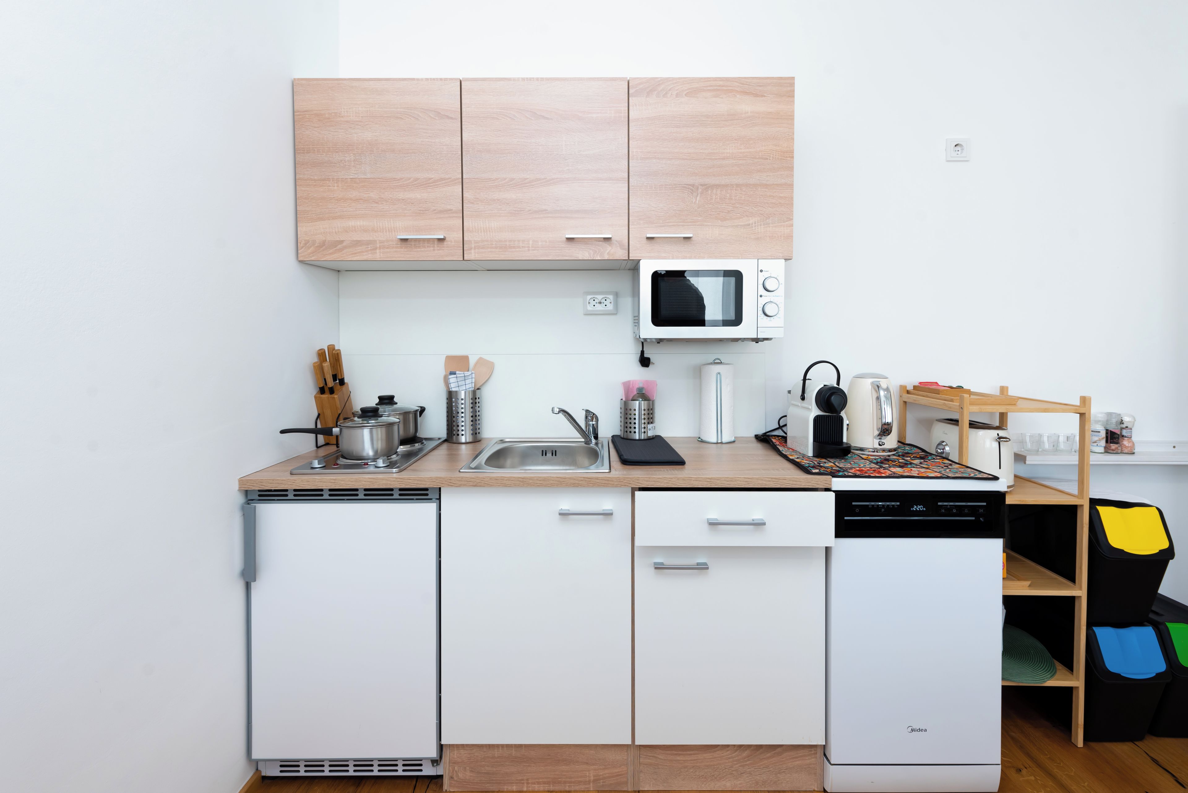 Una cucina compatta con elettrodomestici bianchi, mobili in legno e un forno a microonde.