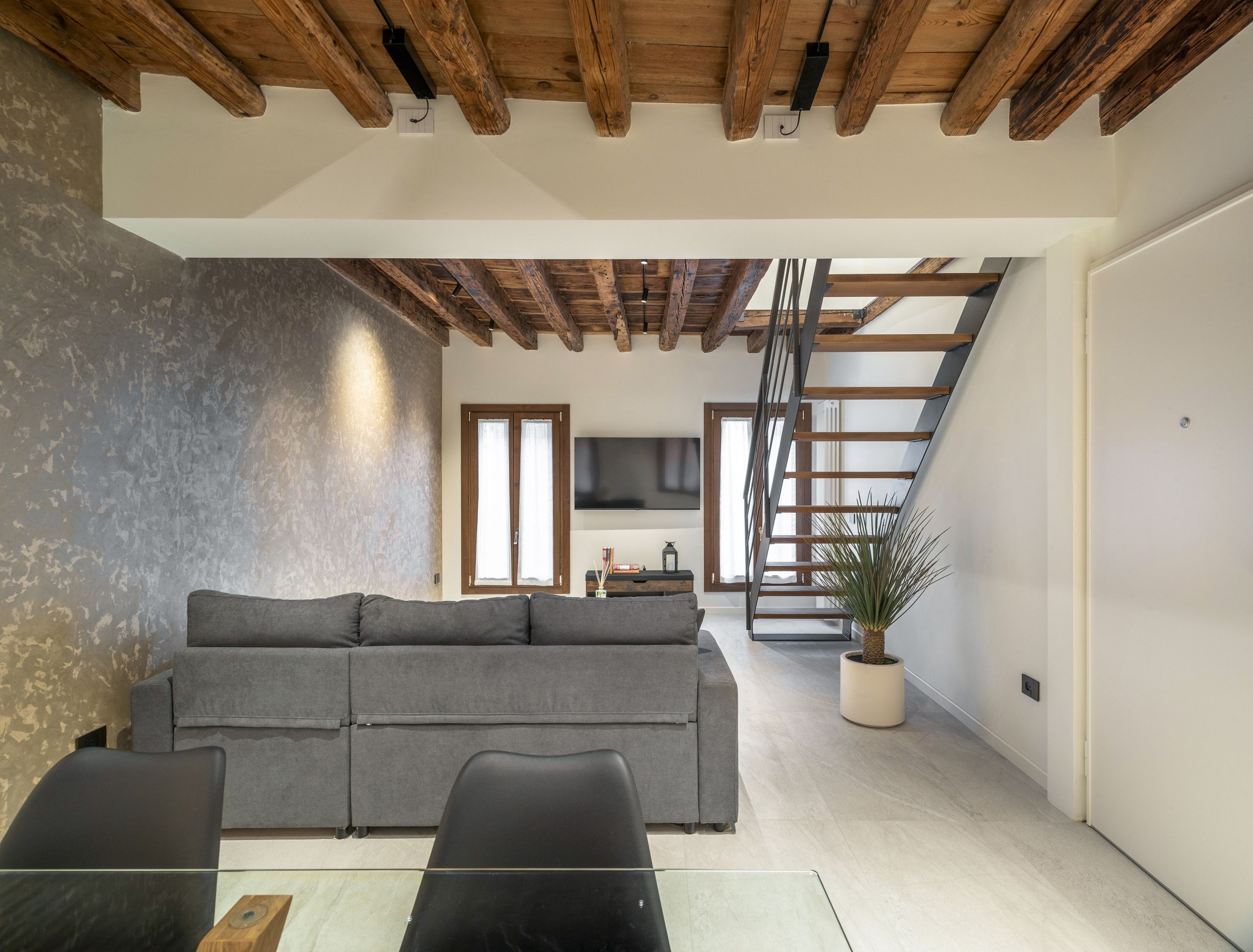 Un salon moderne avec un canapé gris, un plafond en bois et un escalier menant à un niveau supérieur.