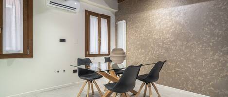 Un espace repas moderne avec une table en verre, des chaises noires, des poutres en bois et un mur à texture.