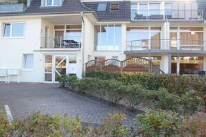 A two-story residential building with a covered entrance, a balcony on the upper floor, and a paved driveway. - Holiday apartment with 1 bedroom (Bad Zwischenahn)