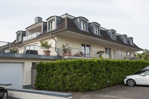 Une maison à deux étages avec un balcon, un garage et une haie bien entretenue.